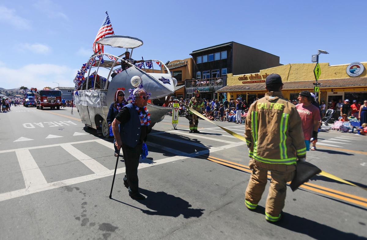 Hundreds of people lined the streets for the annual 4th of July Parade held in downtown Cayucos. A submarine replica float belonging to the Cayucos Citizens’ Advisory Council caught fire while traveling down South Ocean Avenue in the parade. John Carsel, president of the council said the transmission caught on fire. The float itself was not damaged. Carsel laughed, “I didn’t expect to get in the newspaper this way!” Cal Fire firefighters who were in the parade converse with Carsel.