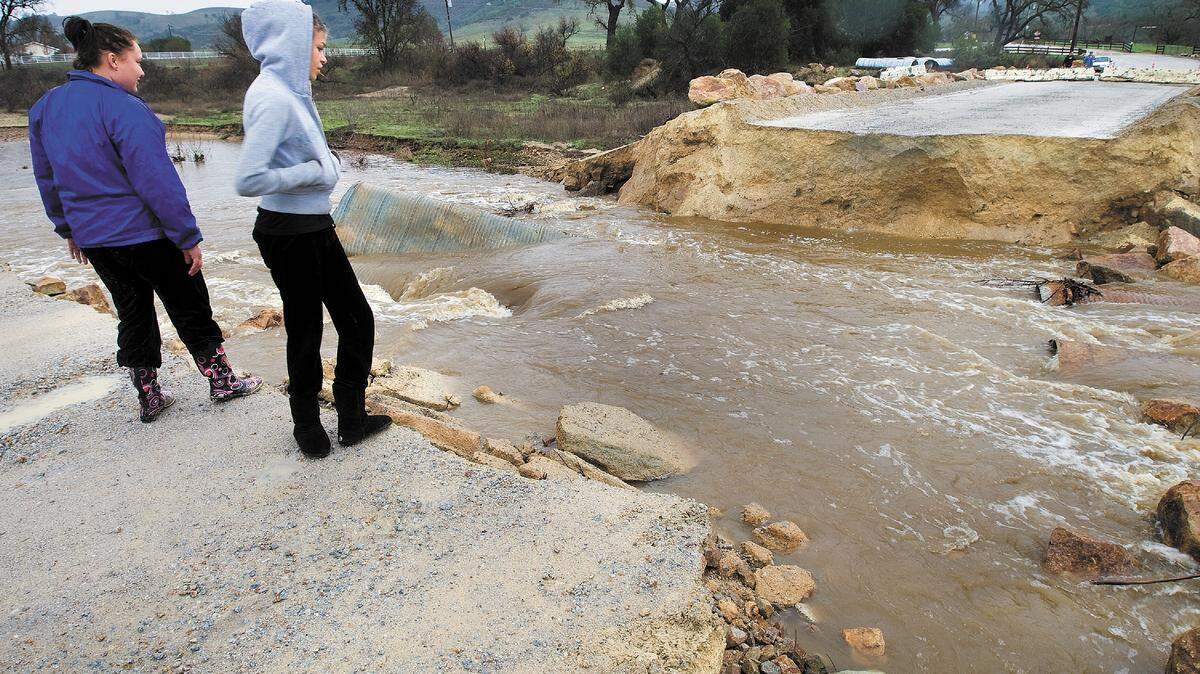 Jessica Espinosa, left, and her friend, Brittany Gibbins, stand on the edge of a washed out section
of Halcon Road in Atascadero.