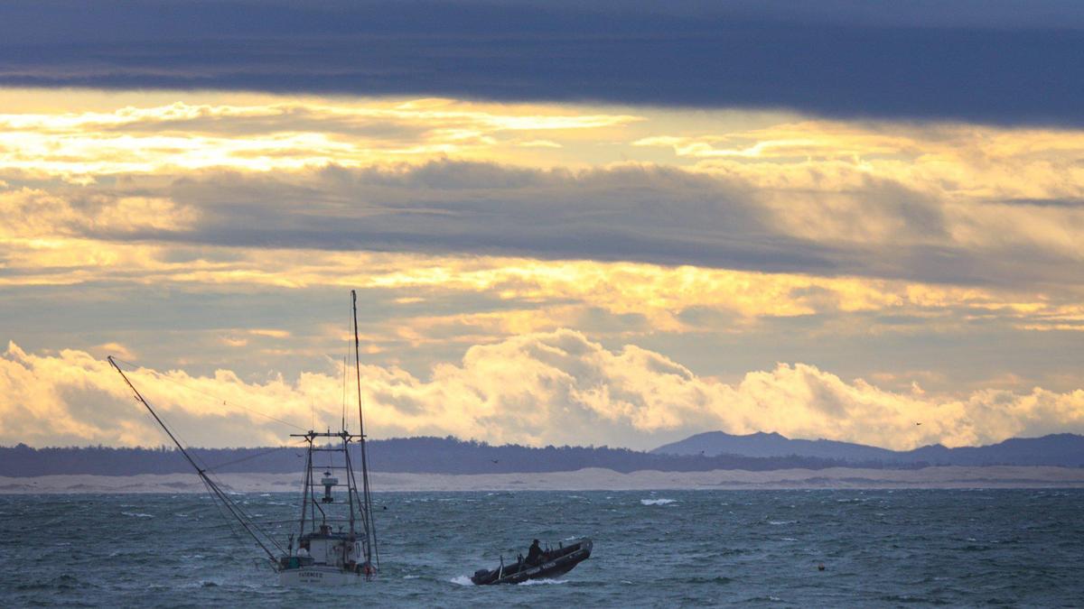 Boats at anchor rocked in choppy surf as a man in an inflatable boat powered through the Port San Luis harbor just after sunrise. A bit of sunlight slipped through from the east at sunrise while clouds from a strong winter storm gathered in the west on Jan. 4, 2023.