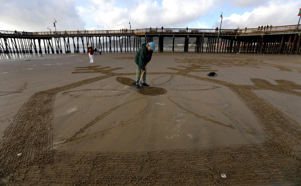 Shelley Evans, of Bakersfield, etches her snowflake cutout on Pismo Beach near the Pismo Beach Pier, Saturday, Dec. 14, 2024. Beachgoers turn Pismo Beach into a seaside winter wonderland at a “Snowflakes on the Sand” event.
