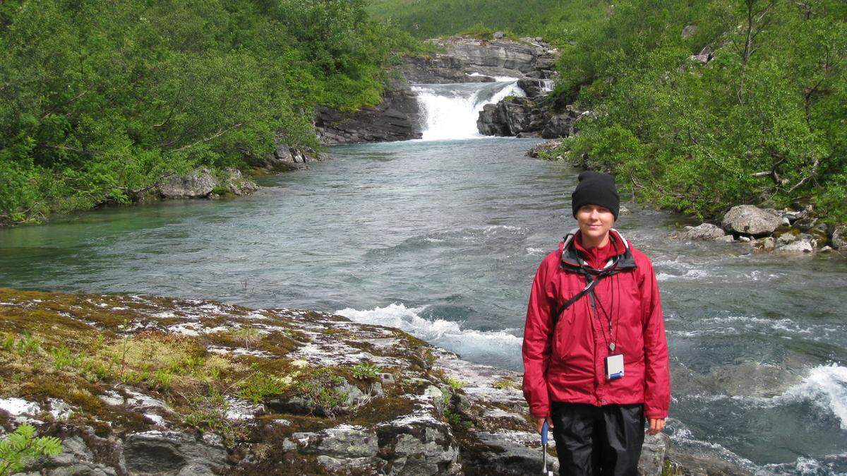 Woman in a hat standing in front of a stream 