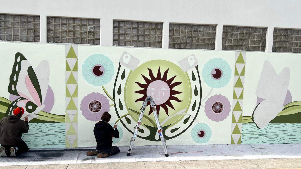 From left, Christopher Norton and Shelby Lowe, owners of the Canned Pineapple commercial art firm in San Luis Obispo, put finishing touches on a mural at the corner of Bridge and Main streets in Cambria. It’s the first of three community murals they’ll create for Visit SLO CAL.