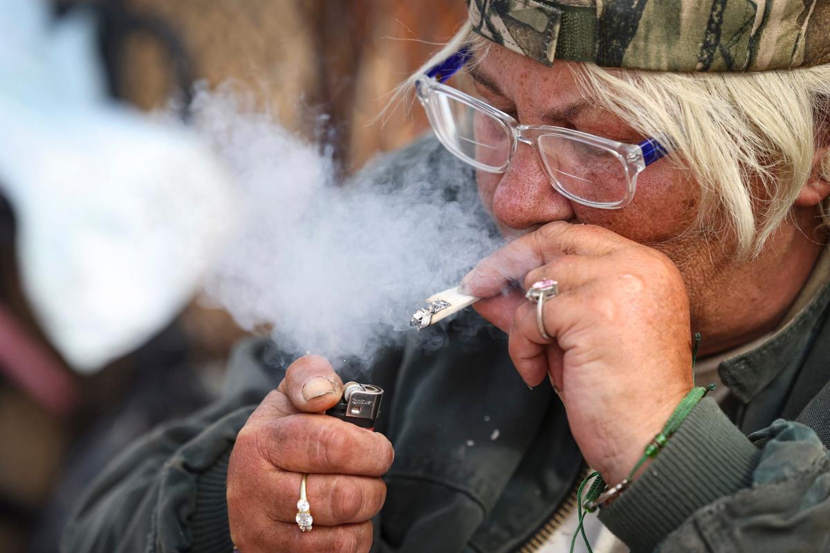 Nena Kosbab-Jones smokes pipe tobacco using note paper to roll it. She was on the Bob Jones Trail near San Luis Creek, a short distance from 40 Prado Homeless Services Center, on Oct. 9, 2024.
