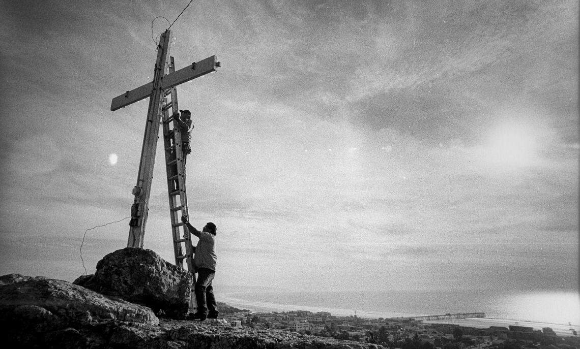 Pismo Beach Public Works employee Clyde Miears replaces Christmas lights on Boosinger park cross, while fellow employee Ray Torres steadies ladder on Dec. 6, 1988. 