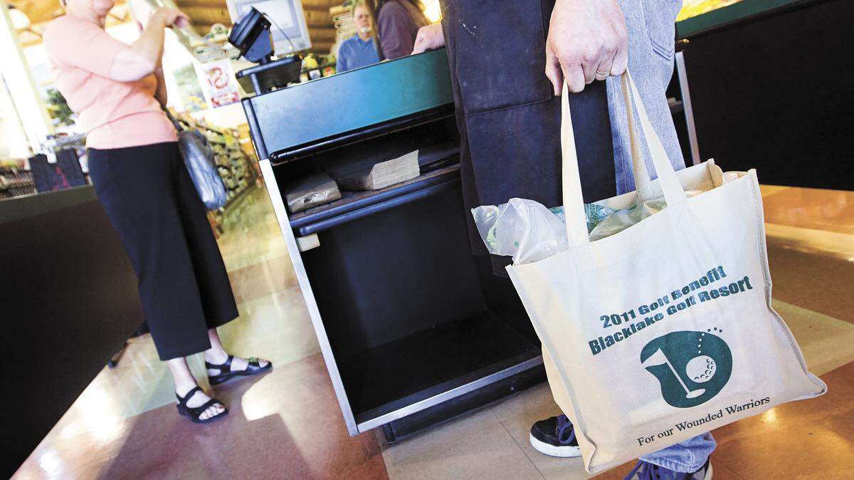 Marten VanBeveren, right, manager of J.J.’s Market in Arroyo Grande, holds a reusable bag full of Rebecca Horner’s groceries as he waits to help her to her car during the first day of the county’s plastic bag ban.