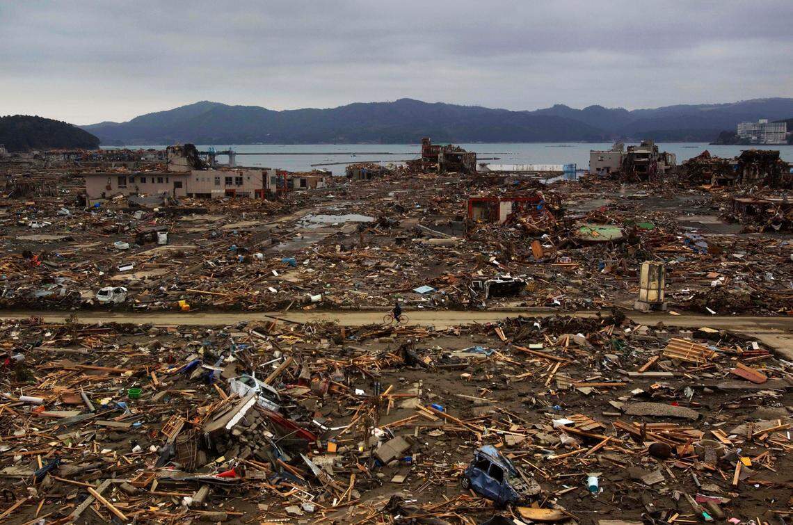 FILE - In this March 15, 2011, file photo, a Japanese survivor of an earthquake and tsunami rides his bicycle through the leveled city of Minamisanriku, Miyagi prefecture, northeastern Japan. March 11, 2021 marks the 10th anniversary of the massive earthquake, tsunami and nuclear disaster that struck Japan’s northeastern coast. (AP Photo/David Guttenfelder, File)