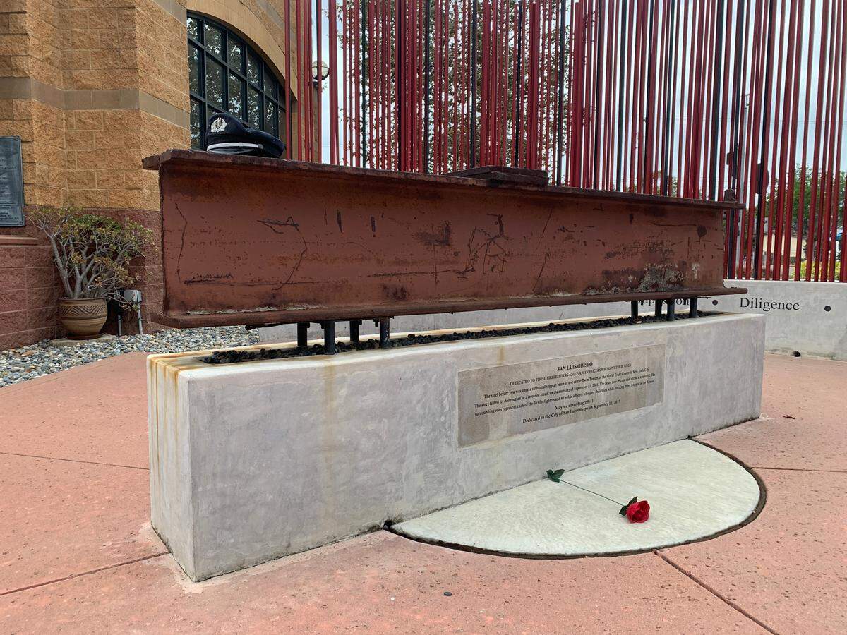 A red artificial rose lies in front of the steel beam at the center of the World Trade Center Memorial in front of Fire Station No. 1 in San Luis Obispo on Sunday, Sept. 11, 2022. A battered American Airlines pilot hat rests on top of the memorial. 