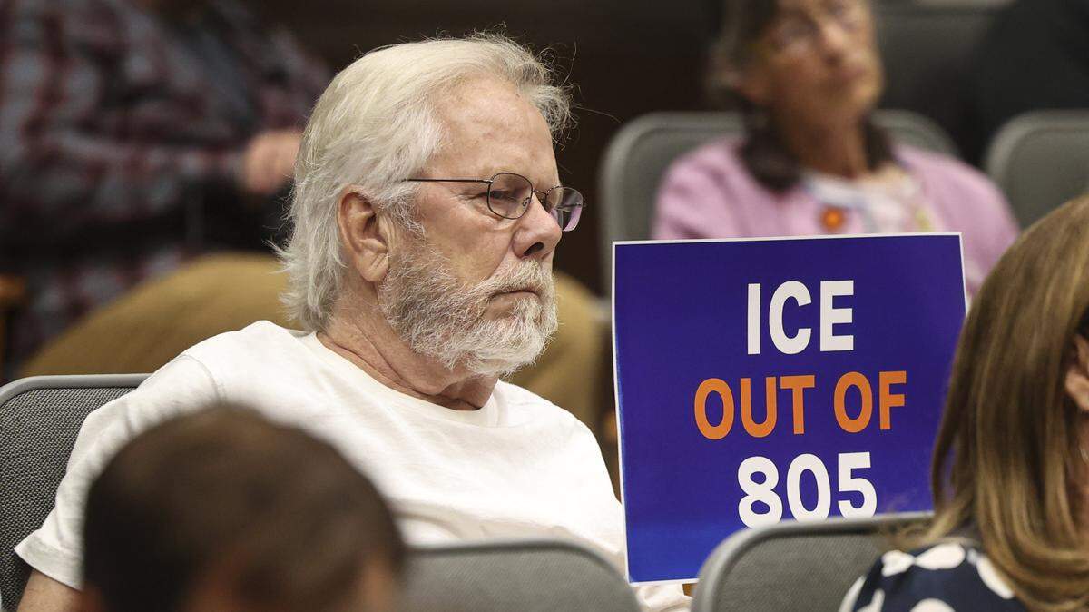 Neil Burke holds a sign facing the board. The San Luis Obispo County Board of Supervisors took public comment and official presentations on a controversial federal grant, seen here on Aug. 5, 2025.