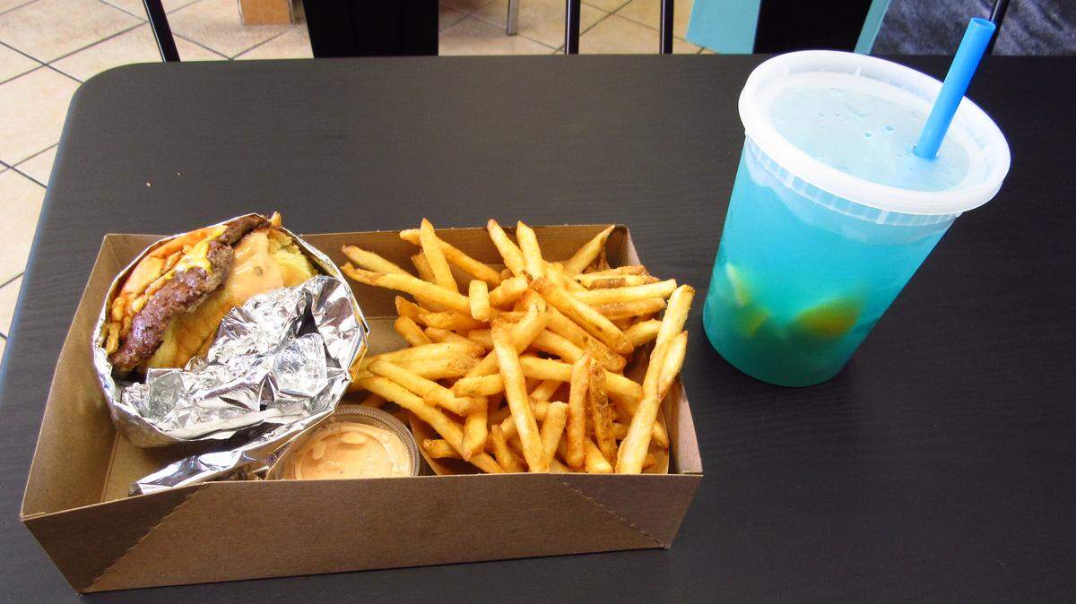 A single smash burger from Low Tide Spot in Pismo Beach accompanies a basket of tallow fries and a blue raspberry smashed lemonade.