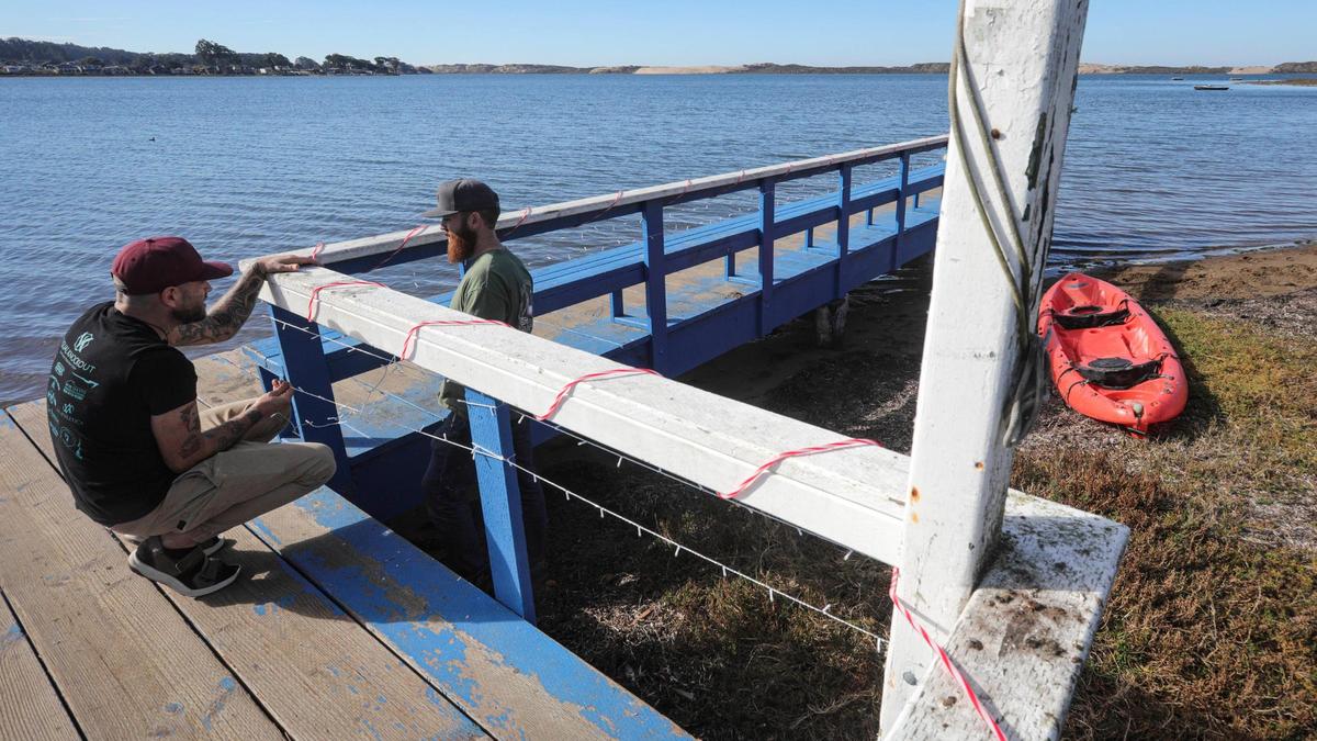 Todd La Velle, left, and Curtis Armstrong string holiday lights on the pier in Baywood on Dec. 5, 2024. About 538 acres of the Morro Bay Estuary sea floor, seen behind them, are listed for sale at an asking price of $7 million.