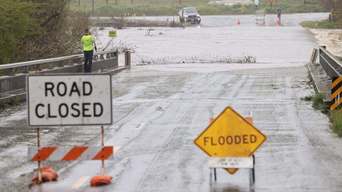 Alex Farrington (left) with PG&E documents road closure as San Luis Creek flooding closes San Luis Bay Drive at Monte Road on March 10, 2023. A traveler on the other side does the same.