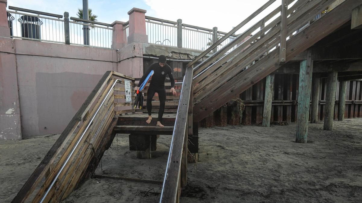 Heavy surf and high tides at Pismo Beach in the last week of 2023 damaged stairways from the boardwalk to the sand, seen here Jan. 3, 2024. A body boarder who gave his name as Fielding hops down a staircase that has been marked closed.