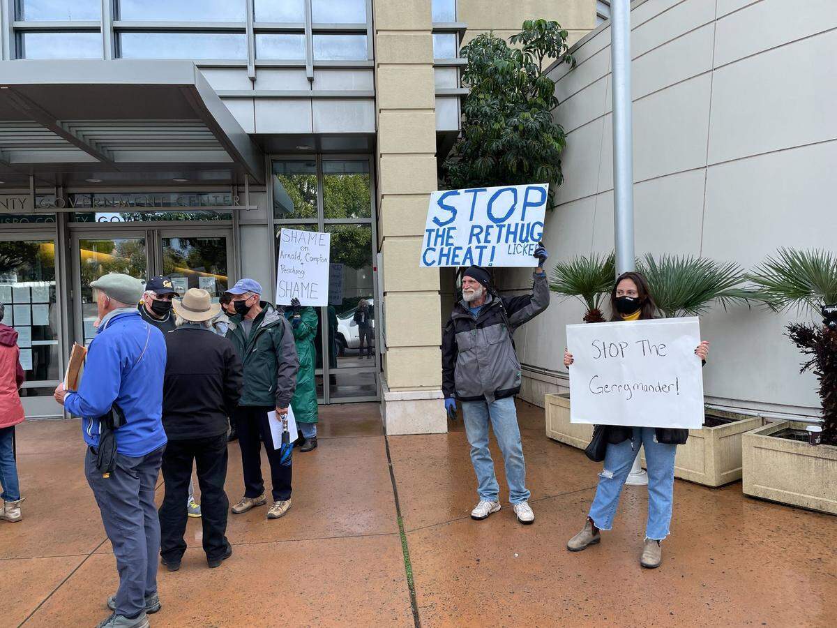 Protesters hold signs outside the Board of Supervisors Chambers on Tuesday, Dec. 14, 2021, as it voted to formally adopt the Patten redistricting map.