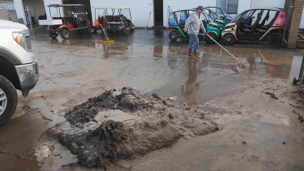 Jeff Babb, owner of Central Coast Carts in Morro Bay at right, pushes mud across parking area. Storm updates Jan 16, 2023, as a series of atmospheric river storms hit the coast.