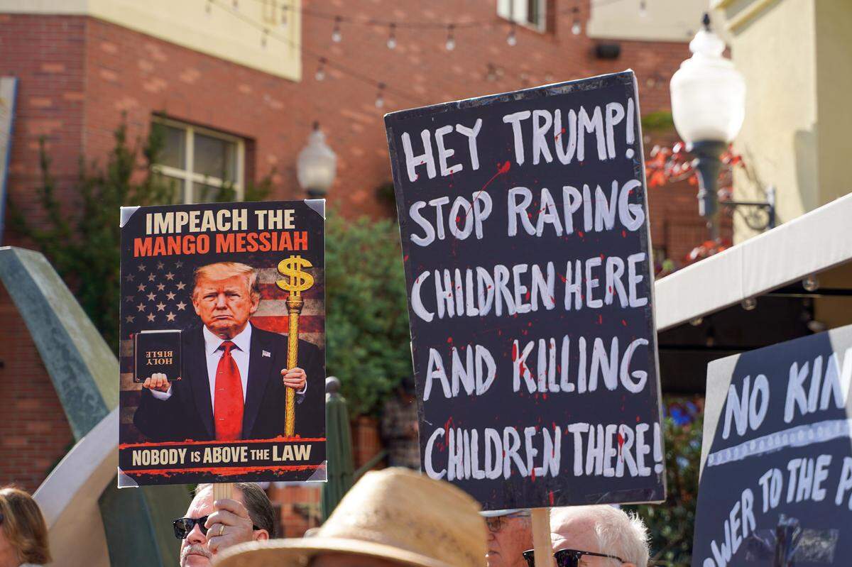 Signs draw attention to President Donald Trump's appearance in the Epstein files and assault on Iran No Kings protest in San Luis Obispo on Saturday, March 28, 2026. Organizers estimated around 2,500 people attended the San Luis Obispo protest, with more in Atascadero, Cambria and Grover Beach.