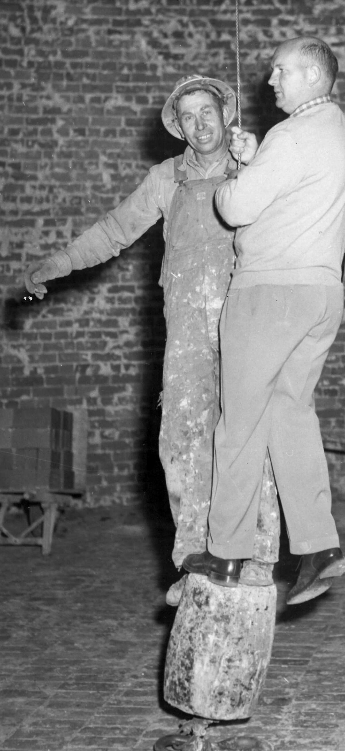 Telegram-Tribune photographer Fen Truebridge mounts the cable elevator, right, with steeplejack Orval Ady of Seattle for the trip up inside the huge brick-lined funnel at the Morro Bay Power Plant. The concrete block allowed only room for one foot and a prayer. First published March 5, 1955.