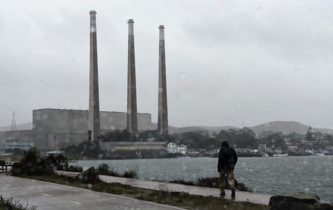 A person takes a rain-soaked walk in Morro Bay on Thursday, Jan. 28, 2021, with the closed Duke Energy power plant in the background.