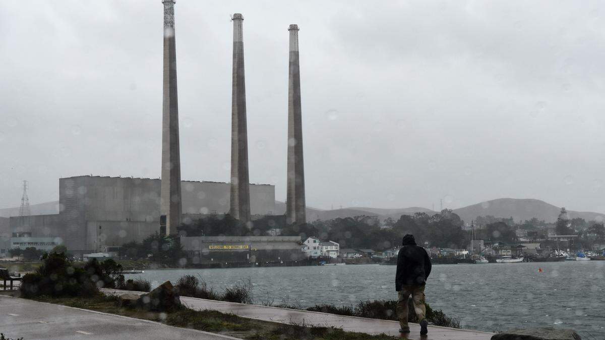A person takes a rain-soaked walk in Morro Bay on Thursday, Jan. 28, 2021, with the closed Duke Energy power plant in the background.