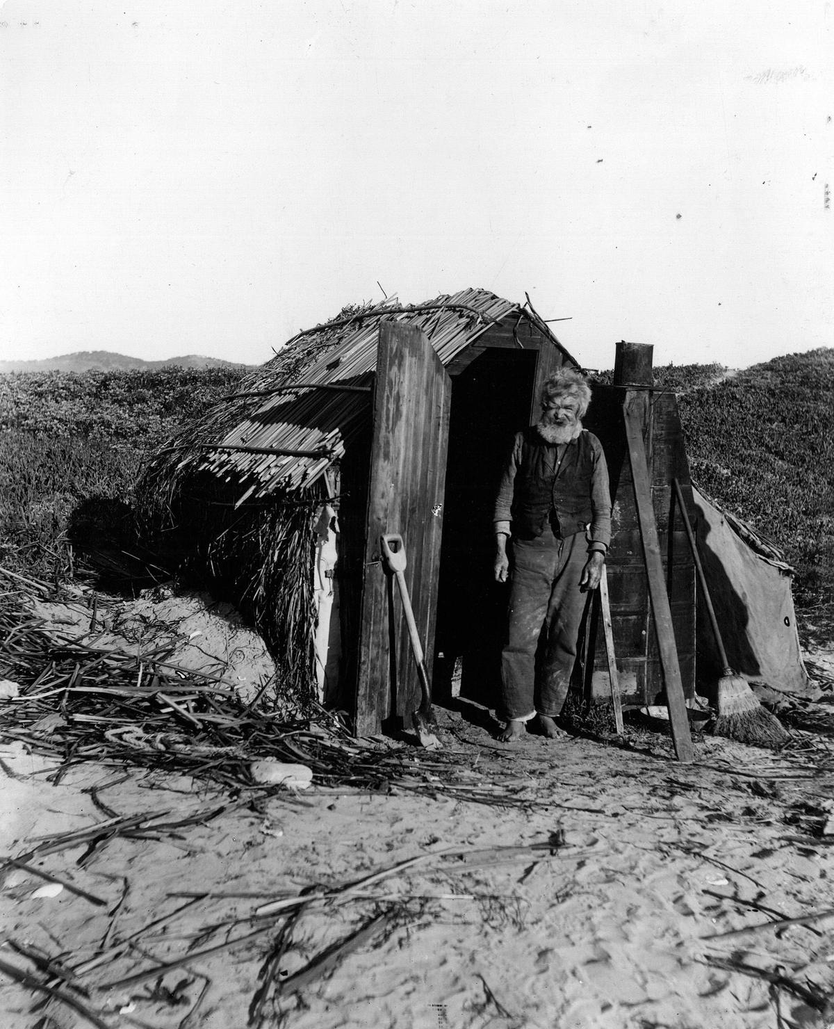 Sometimes the clipping is not with the photo in the files. Pity. This man has a story to tell. Standing barefoot in the sand a bearded man squints at the photographer. A shack with a tule roof and sides of thatched tules and canvas tent. Heat is provided by a tin stove that looks to be made of recycled material. A shovel and broom at the ready to push back the always blowing sand. In pencil on the back of the print is a numeric code and “John Bell—Old hermit of Pismo Beach 1901” The photo ran 4 columns wide x 8 1/2 inches tall on page 8 of a Saturday edition of the Telegram-Tribune. It is also marked “PE” or “RE” though at this time I don’t know what that notation refers to. I am guessing that it ran in paper sometime the 60s or 70s. Both Effie McDermott and Norm Hammond, South County authors who have written about dunites currently have not come across John Bell. The photo was stamped part of the C.C. Pierce collection of historical photographs, then that citation was crossed out and replaced with: PLEASE CREDIT Title Insurance and Trust Company (LOS ANGELES) Collection of Historical Photographs Their website has the same photo and variations but no more information. There are 55 John Bell listings in California in the 1900 census but none are from San Luis Obispo County.