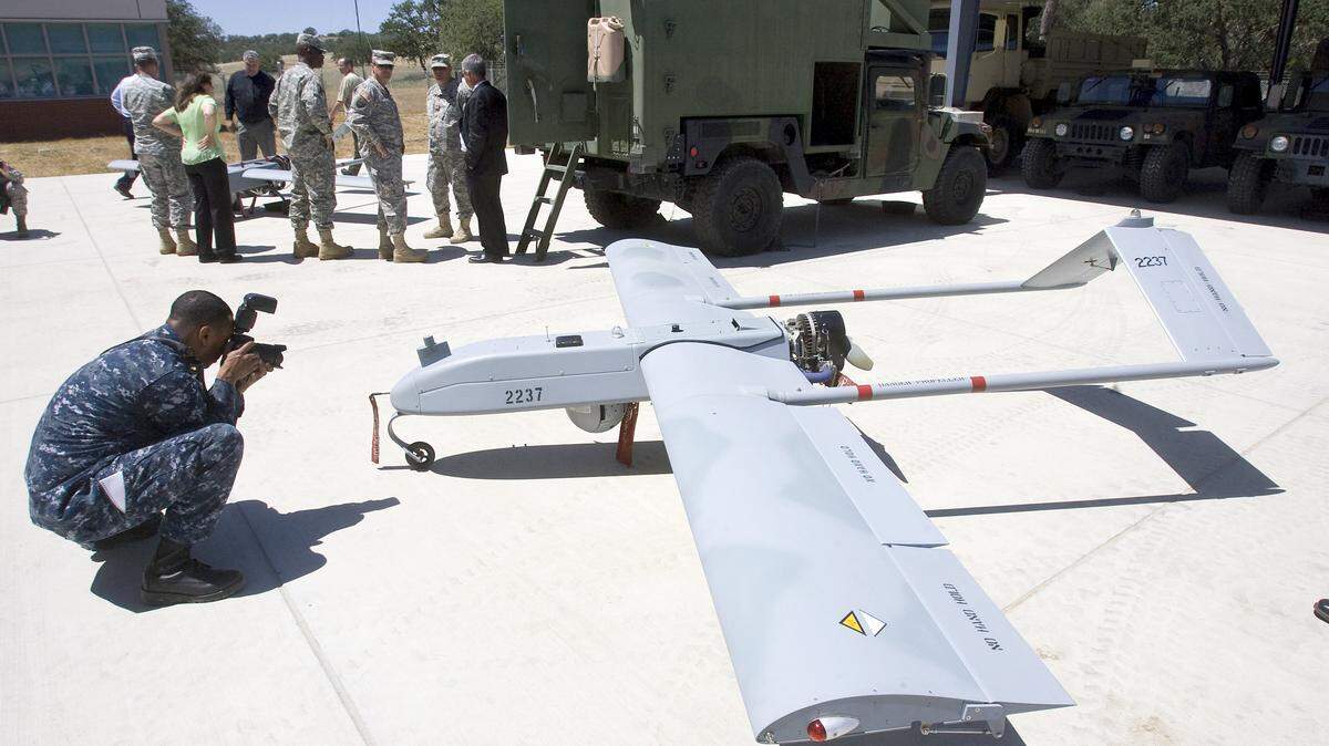 U.S. Navy Mass Communication Specialist 2nd Class Shawn W. Stewart takes a picture of a RQ7B Shadow 200 unmanned aircraft. The truck in the background controls the aircraft for an up to 6-hour flight.