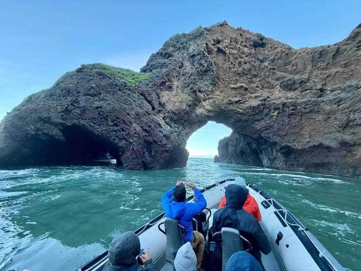 A 30-foot zodiac operated by Pacific Offshore Expeditions approaches a sea arch during an orca quest in the Santa Barbara Channel in January 2026.