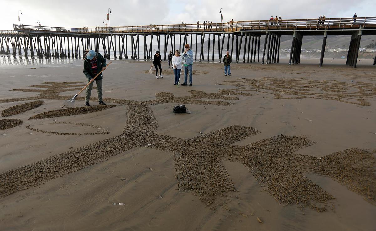 Shelley Evans, left, of Bakersfield, etches her snowflake cutout on Pismo Beach near the Pismo Beach Pier, Saturday, Dec. 14, 2024. Beachgoers turn Pismo Beach into a seaside winter wonderland at a “Snowflakes on the Sand” event