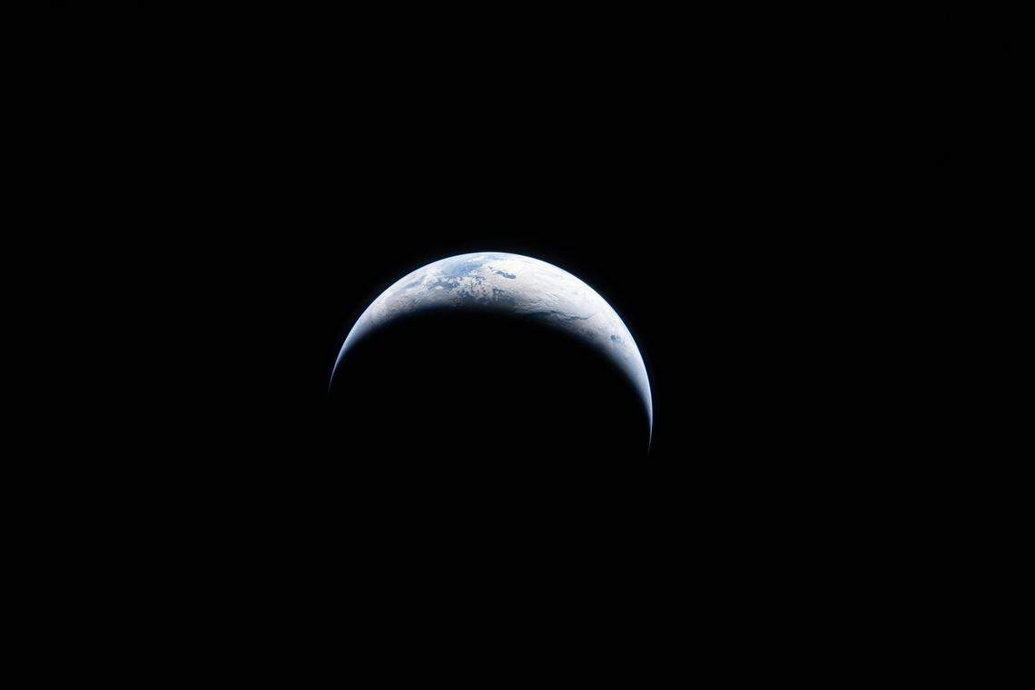 Earth is illuminated against the blackness of space in this photo taken by an Artemis II crew member through an Orion spacecraft window on April 4, 2026.