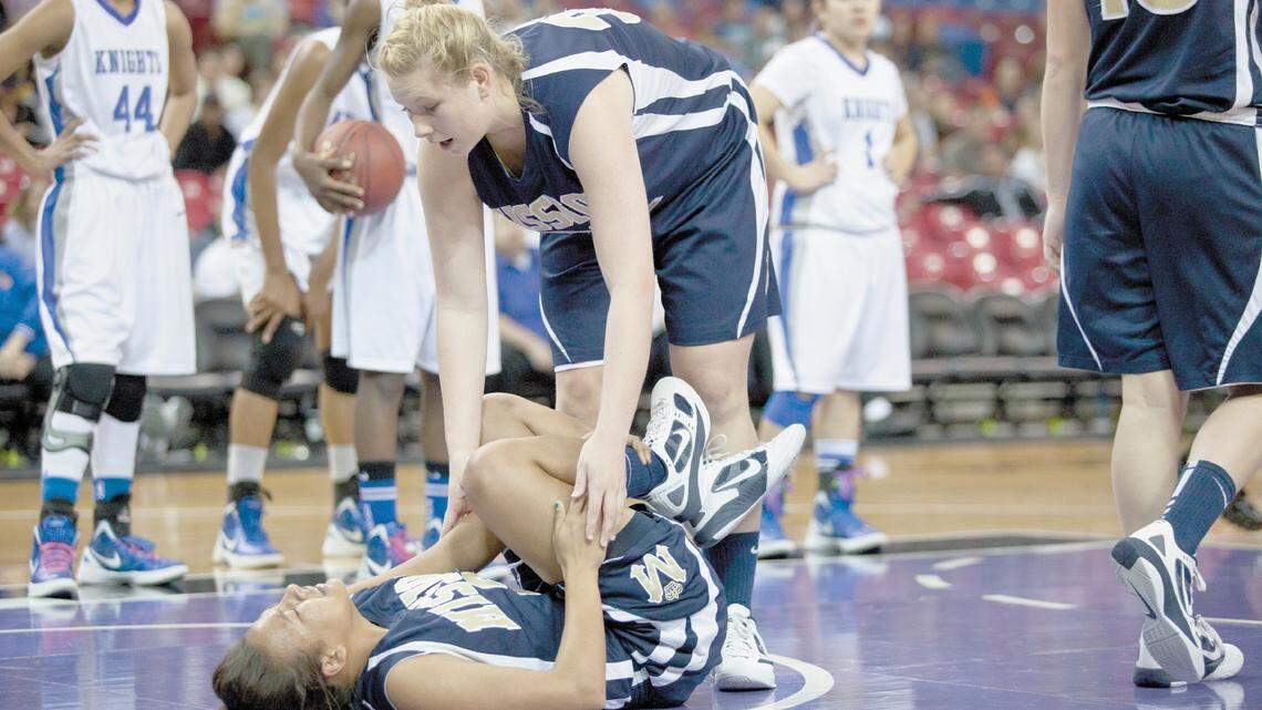 Kaylee Williams, bottom, clutches her ankle after injuring it in the first quarter, while Bri Harvey checks on her in Saturday’s game.