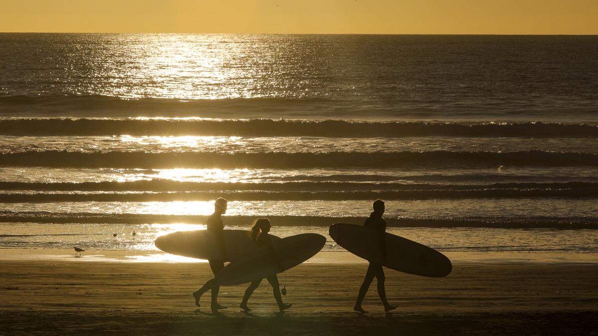 Cal Poly students head out for a sunset surf session in Pismo Beach in January. From the left are Grant Bernosky, McKenna Troje and Sean Quinn.
