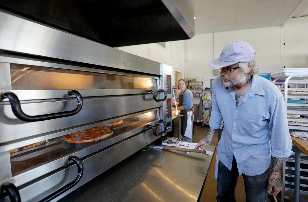 Aaron Coyes, the pizza baker, checks on the pizzas in the oven.