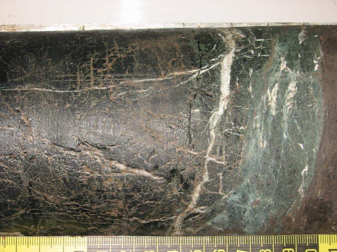 Elongated rock sample that is mostly black with a section of teal-green rock on the right side.