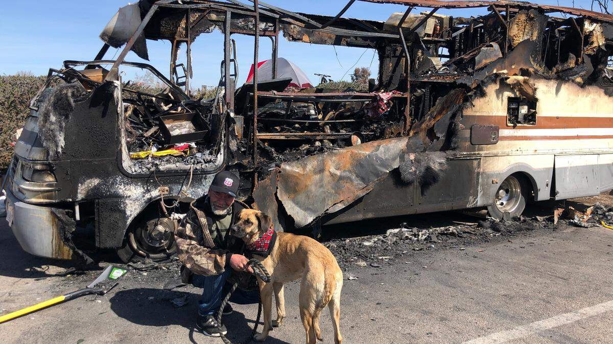 Billy Tosch, 63, with his dog Sadie, 2, pose for a photo in front of their burned recreational vehicle home in the Paso Robles Walmart parking lot. Tosch is temporarily living in the tent seen behind the RV.