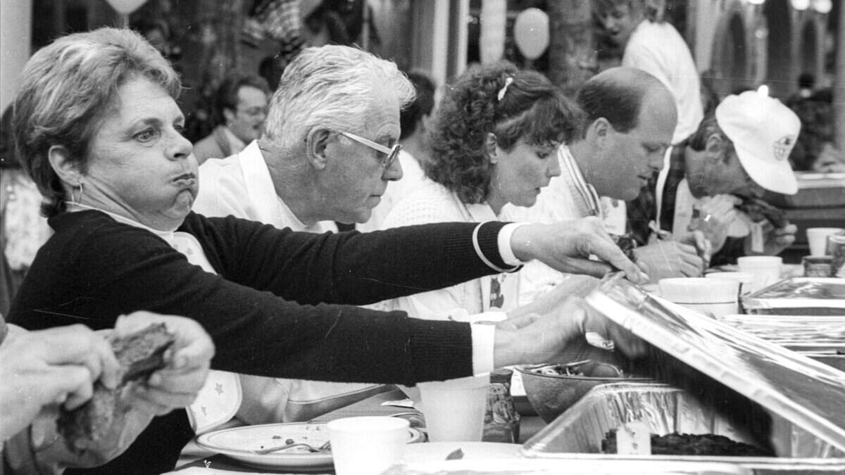 Betsy Camp mugs as she reaches for yet another jucy entry from one of six restaurants competing in the fifth annual Rib Cook-off July 16, 1987. Other judges, from left, were Carl Hysen, Mary McGrgor, Pete Magnusson, and Robert Griffin. There was a split decision for the best ribs. The Judges Award went to Nothing But the Best restaurant while the People's Choice was won by the Old Country Deli.