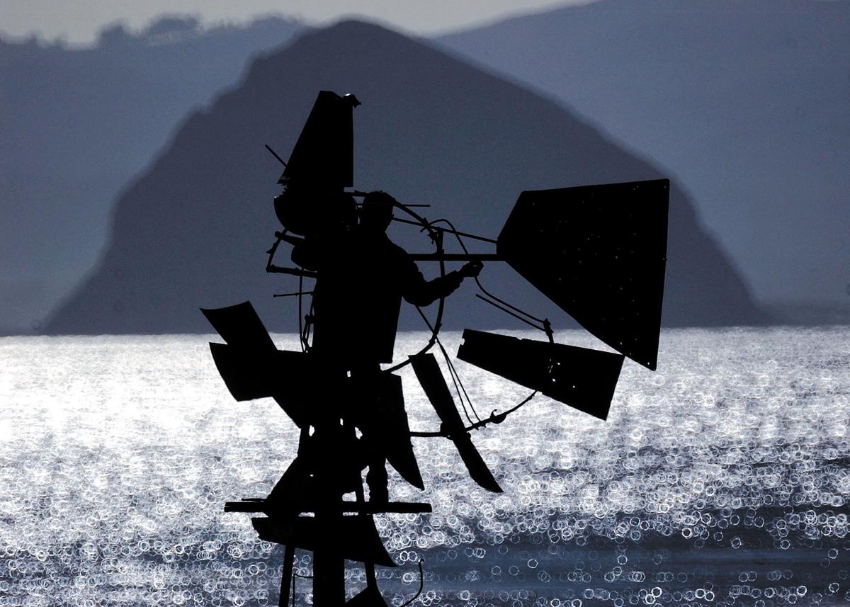 Rocky Poletti of Farm Supply works on a windmill next to Highway 1 north of Cayucos that had been damaged for a number of years. It used to drive a well pump that fed a water trough but the restored windmill will be just for looks. Morro Rock is in background on Nov. 26, 2003.