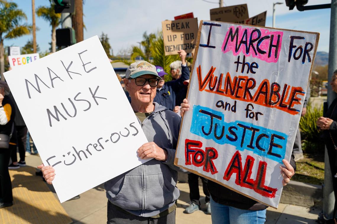 San Luis Obispo residents David Riester, left, and Rebecca Meredith hold signs during a protest on Los Osos Valley Road on Monday, Feb. 17, 2025. Riester said the protest was a good way to show opposition to the second Donald Trump term in-person.