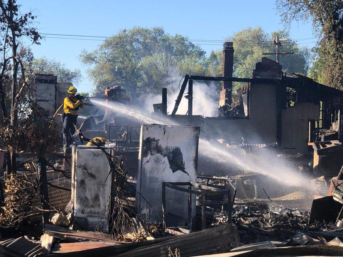 A firefighter douses hot spots at a Paso Robles home destroyed by a fire sparked by weed abatement in the Salinas Riverbed in June 2020.
