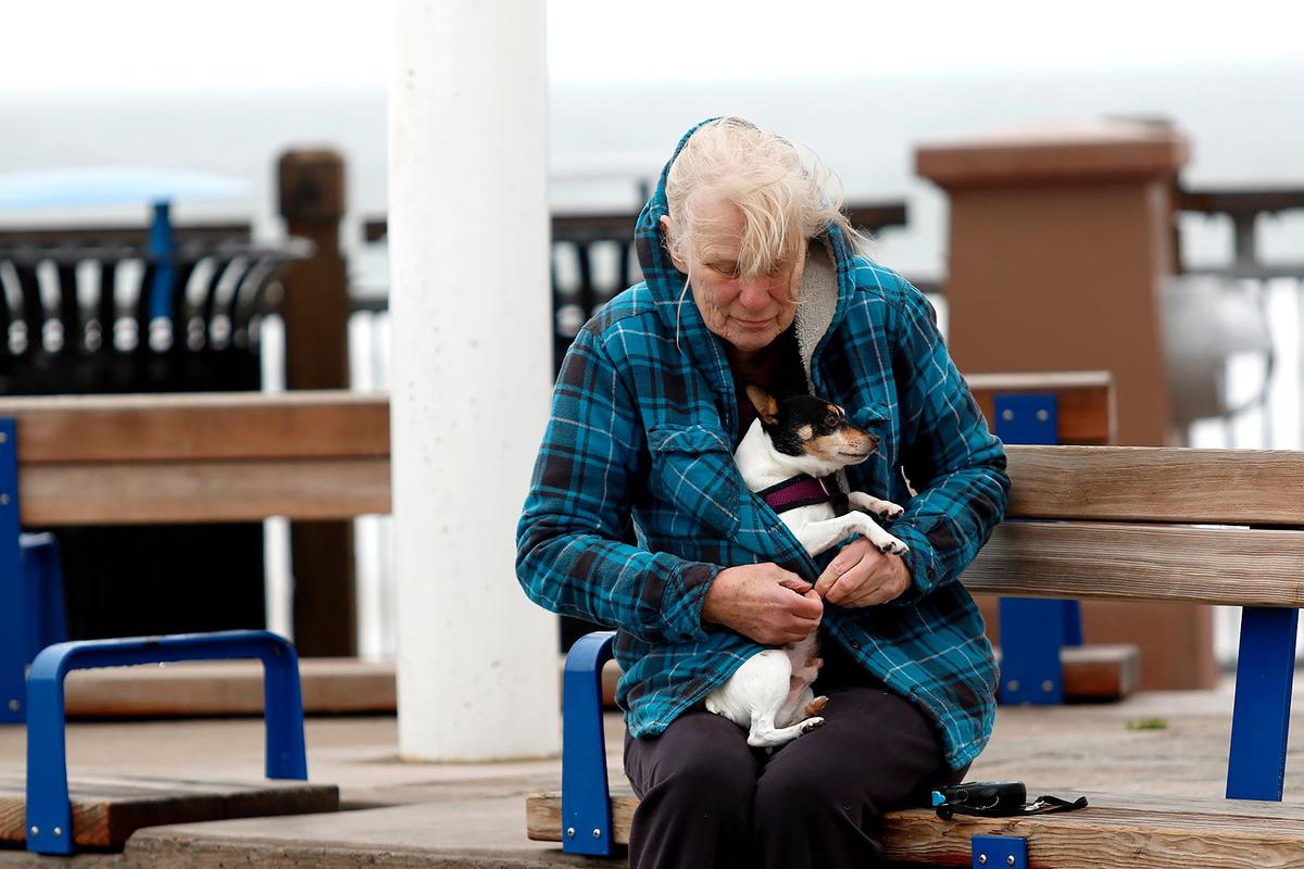 A cold Jana Jones of Arroyo Grande shields her 7-year-old dog Ike inside her jacket on the Pismo Beach Pier. Winds there were gusting up to 30 mph late Saturday morning, Dec 31, 2022.