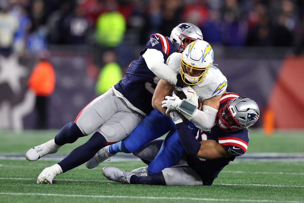 Elijah Ponder #91 and Christian Elliss #53 of the New England Patriots tackle Justin Herbert #10 of the Los Angeles Chargers during the fourth quarter of the AFC Wild Card Playoff game at Gillette Stadium on Jan. 11, 2026 in Foxborough, Massachusetts.