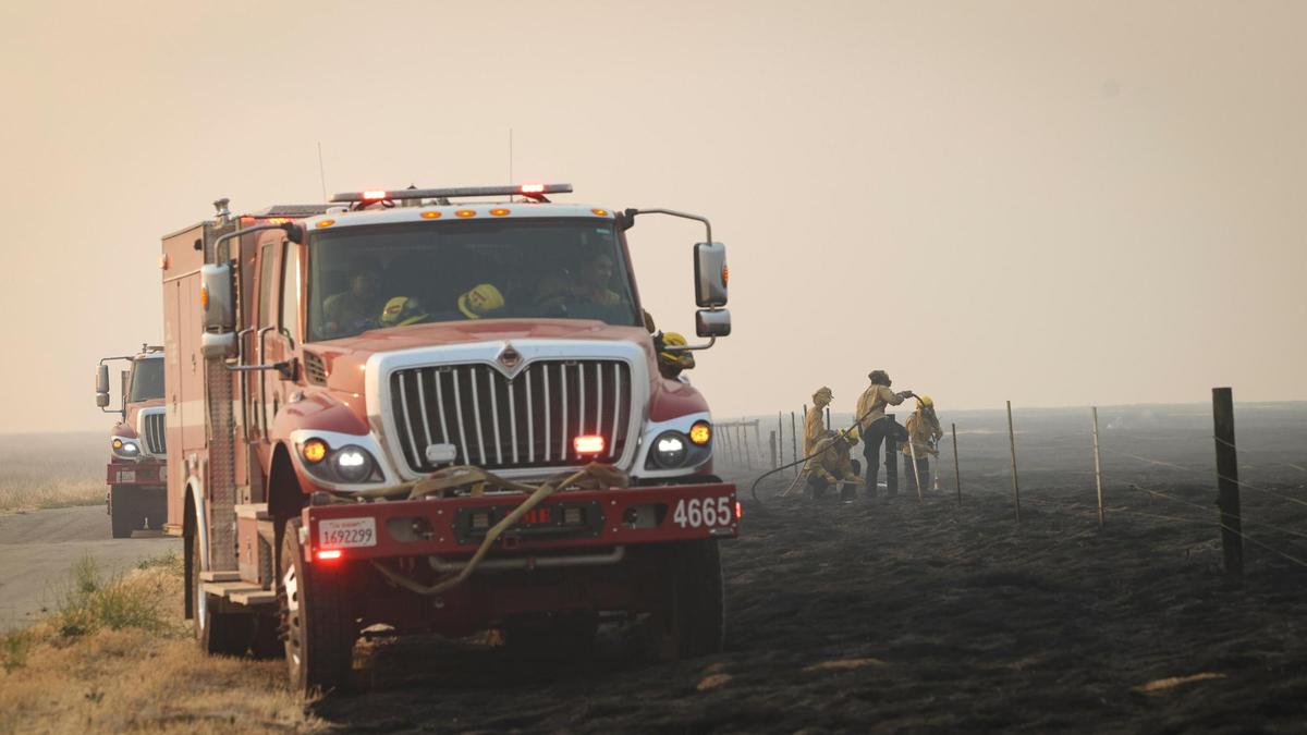 Firefighters from Monterey County extinguish smoldering wood posts on a cattle fence along Soda Lake Road after the Madre Fire burned through the area on July 3, 2025.