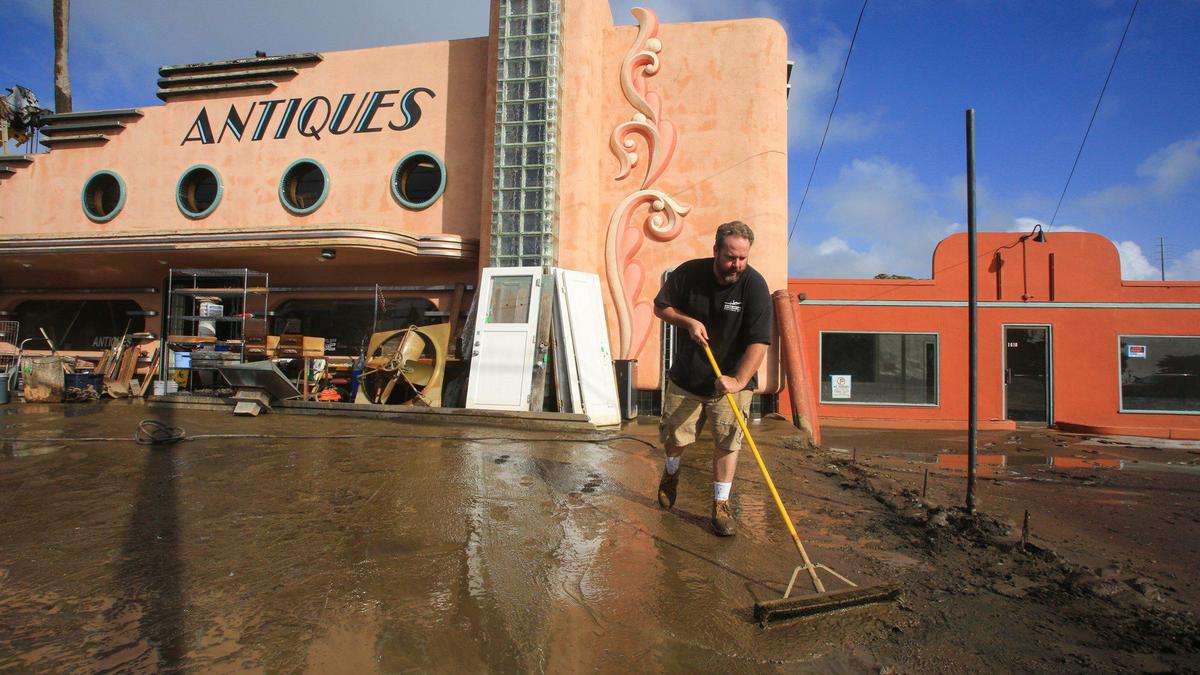 Paige Pollock helps out a friend by using a flipped broom as a mud scraper at Morro Bay Antiques, which was flooded in Monday’s deluge. A break in the storm track on Jan. 10, 2023, allowed hard-hit businesses in Morro Bay to clean up.