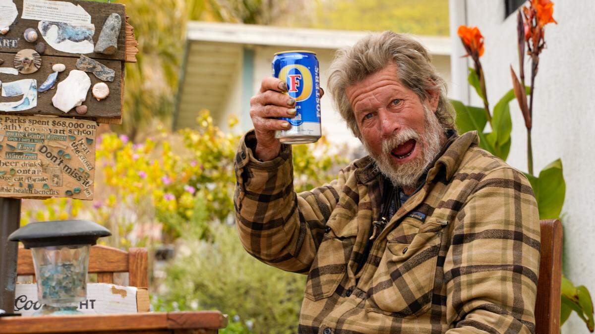 Cowboy, an unhoused resident of Shell Beach, raises a can of Foster’s beer. Cowboy has been homeless for more than 25 years but said he isn’t interested in being housed.