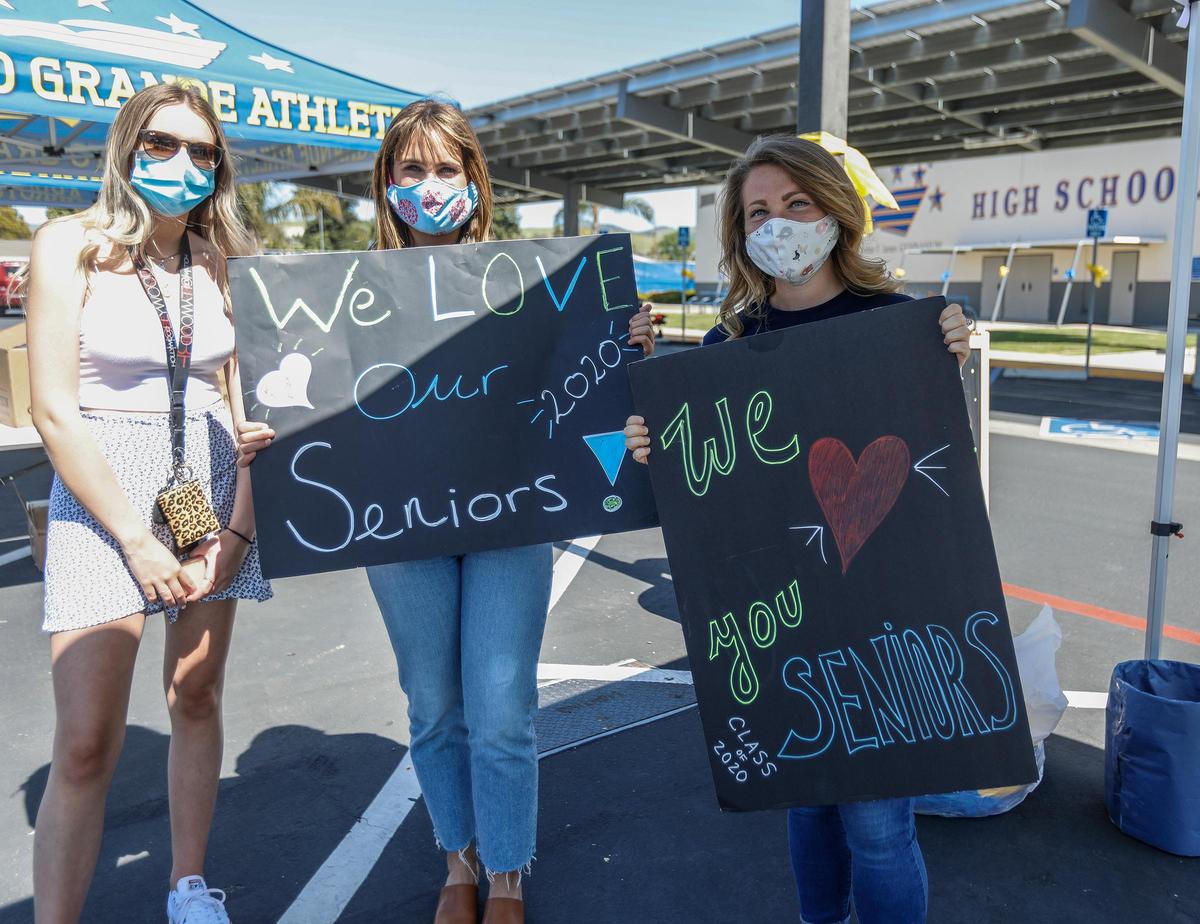 Volunteers cheered students as they arrived to pick up their yard signs from the parking lot at Arroyo Grande High School. From left are AGHS student Larkin Paddack, teachers Santina Olney and Miranda Gasenica holding supportive signs.