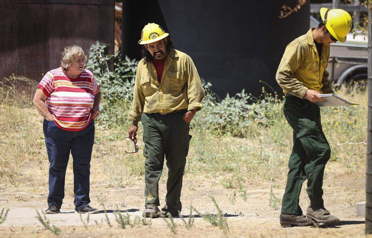 Firefighters from the San Bernadino National Forest contacted residents of Parkhill Road about the evacuation warning. Debra Gonzales talks to firefighters Oscar Gandarilla and Ryan Collins on Aug. 13, 2025.