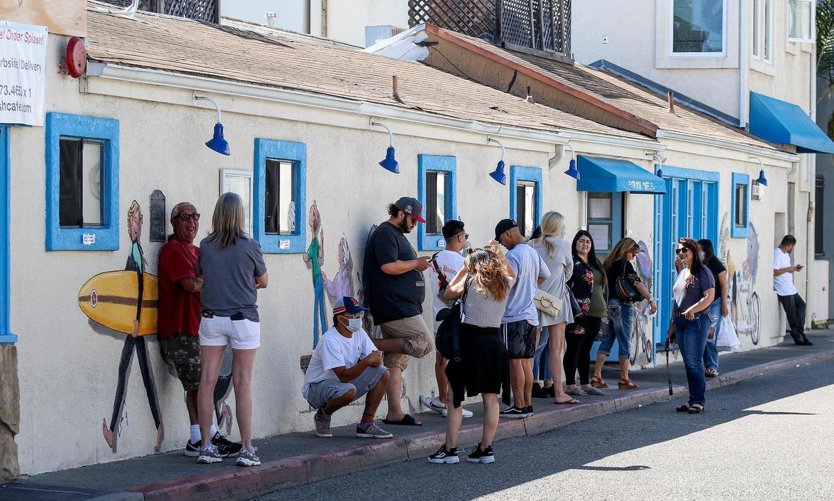 People wait to pick up food at Splash Cafe in Pismo Beach. Hot weather drew big crowds to Pismo on Saturday, despite the county’s stay-at-home order. Many were not using proper social distancing, but a few were wearing masks.