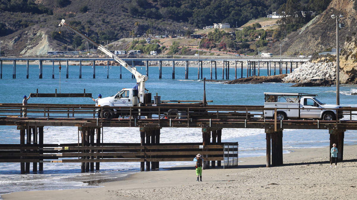 Workers from Port San Luis crane a heavy beam on the Avila Pier in Avila Beach on Monday, Nov. 14, 2022, as beachgoers watch. The Port San Luis Harbor District Board approved a plan to evaluate whether an offshore wind port is suitable in the area.