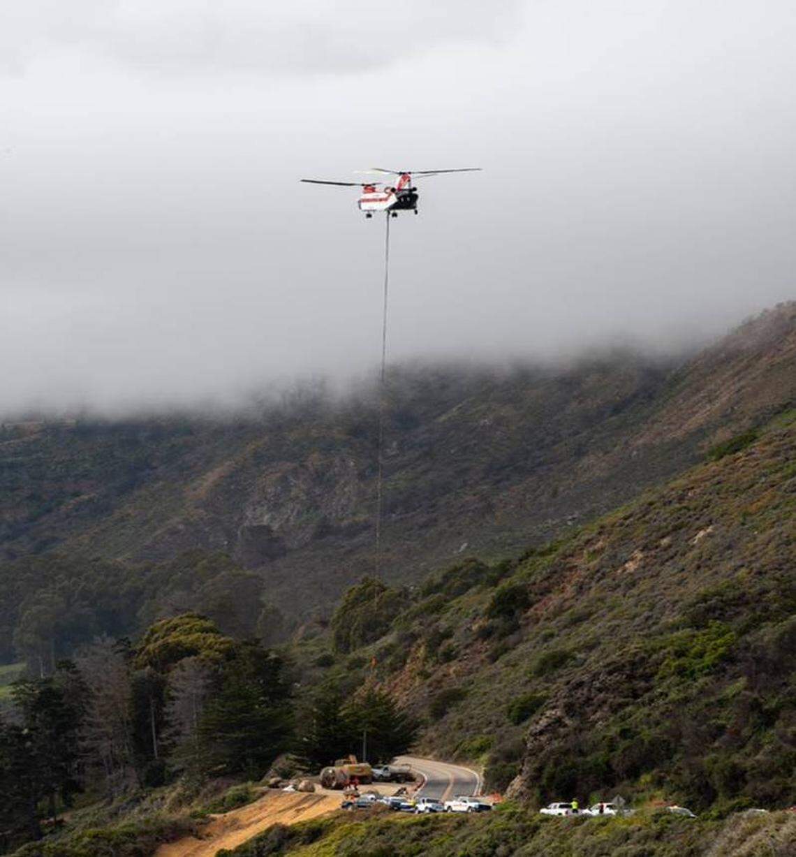 A helicopter carrying 25,000 pounds of Caltrans tunneling equipment is silhouetted against the clouds at Rat Creek near Big Sur on June 22, 2021.
