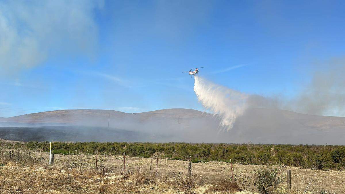 A helicopter drops water on a vegetation fire burning along Highway 1 near South Bay Boulevard in Morro Bay around noon on Nov. 1, 2023.