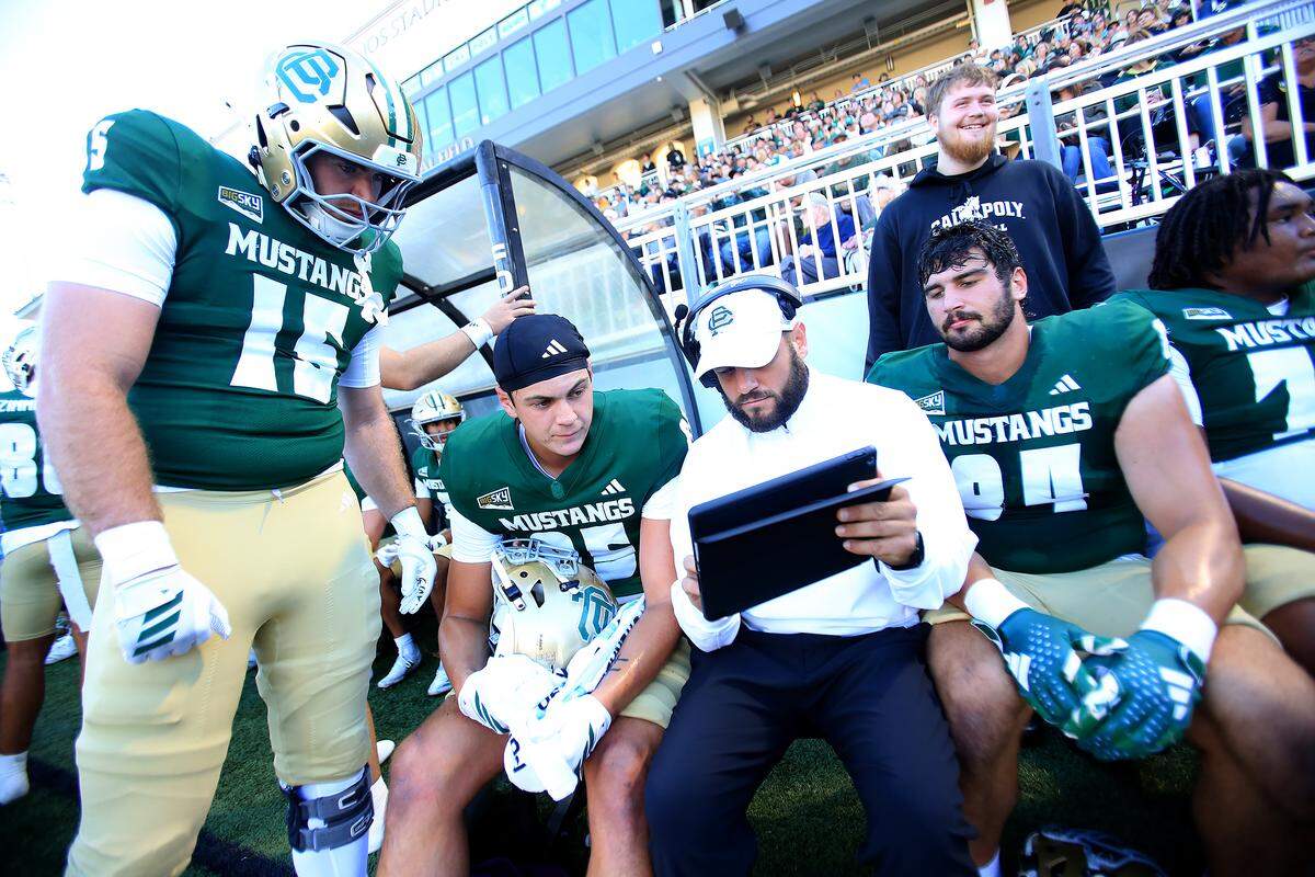 Mustang players Alex Marchall and Nic Sani listen to a coach on the sideline.  Cal Poly lost to UC Davis 34-27 in a college football game at Mustang Memorial Stadium on Oct. 4, 2025.