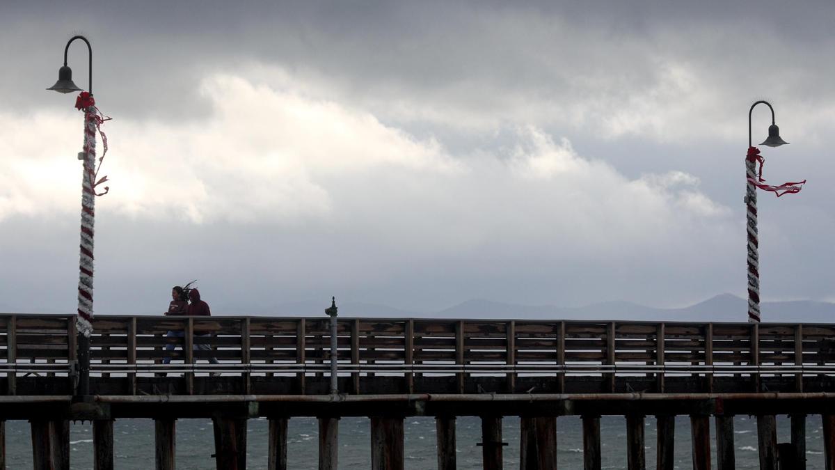 Gray skies and gusty winds blow hair and holiday decorations around on the Cayucos Pier as a storm barrels ashore on Monday, Dec. 13, 2021.