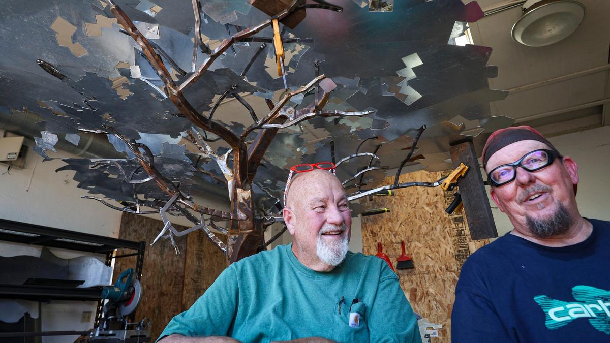 Allen Root, left, and fellow metal artist David Curry, with a large metal tree they have been commissioned to create, on July 10, 2024. Root has been battling late-stage prostate cancer for nearly nine years.